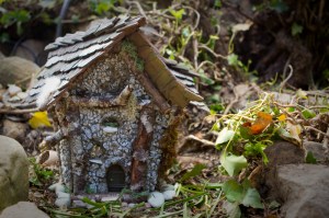 Julie's first fairy house, called Faery's Rest. It is made of gray and white rocks, with a green door and green roof. It is sitting amongst orange nasturtium flowers.