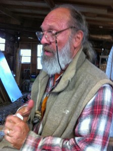 John Crawfore, the master himself, teaching a class. His beard is gray, his hair is pulled back in a pony tail. He wears glasses on a cord that drapes around his neck. He wears a red plaid flannel shirt and gray fleece vest..